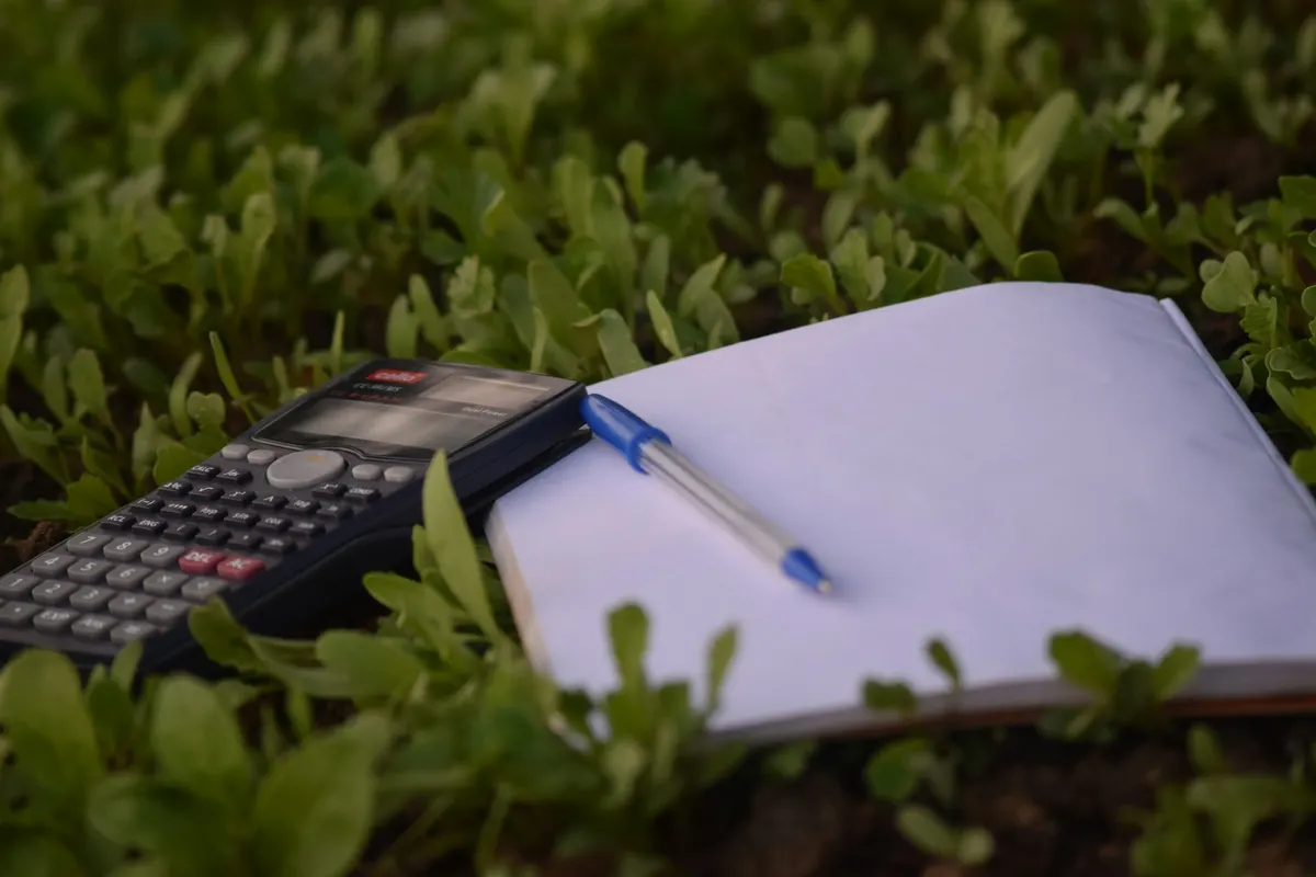 Calculatrice et carnet de notes posés dans une culture, pour chiffrer la rentabilité d'une diversification