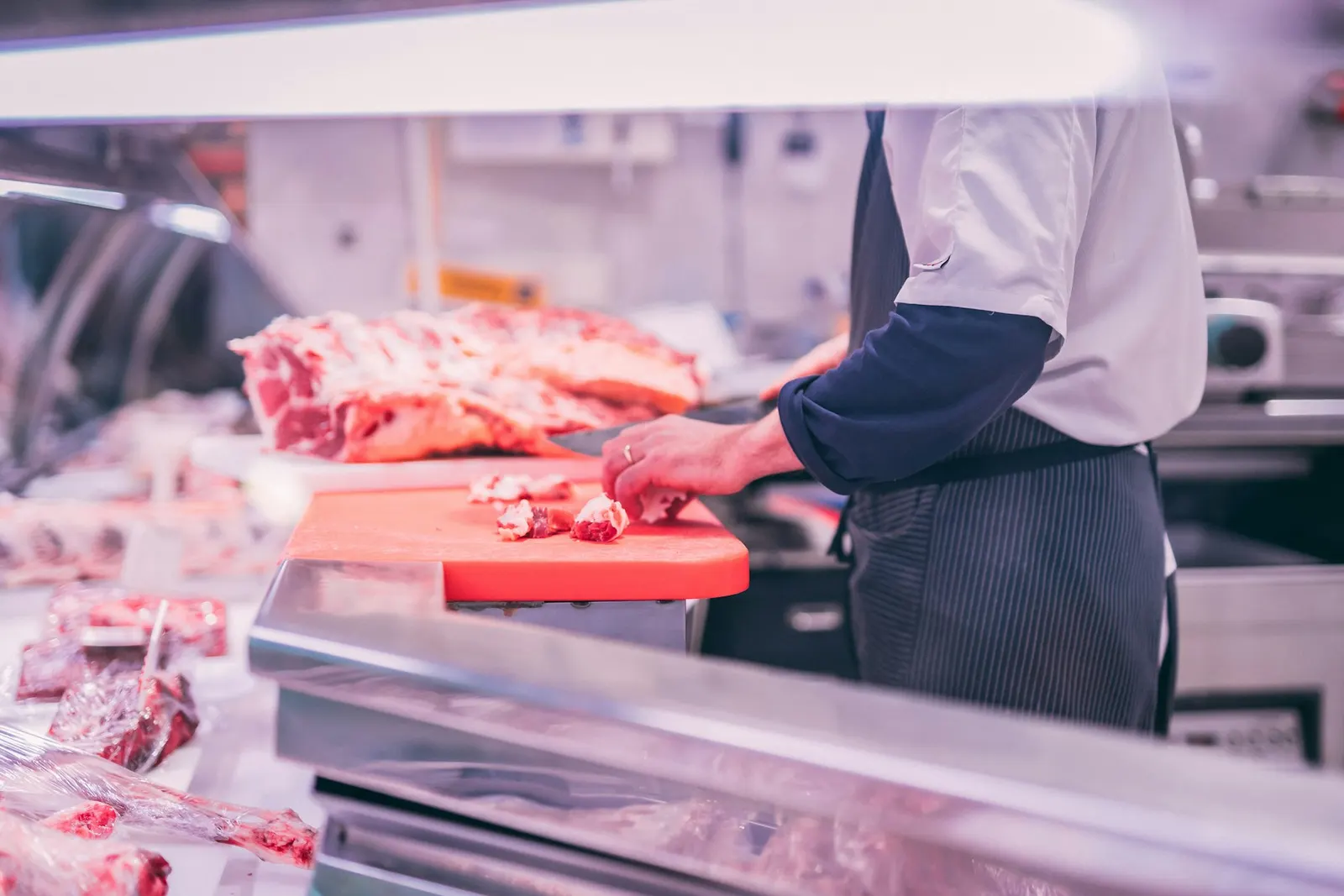 Boucher en tablier découpant de la viande sur une table en inox dans un atelier de découpe