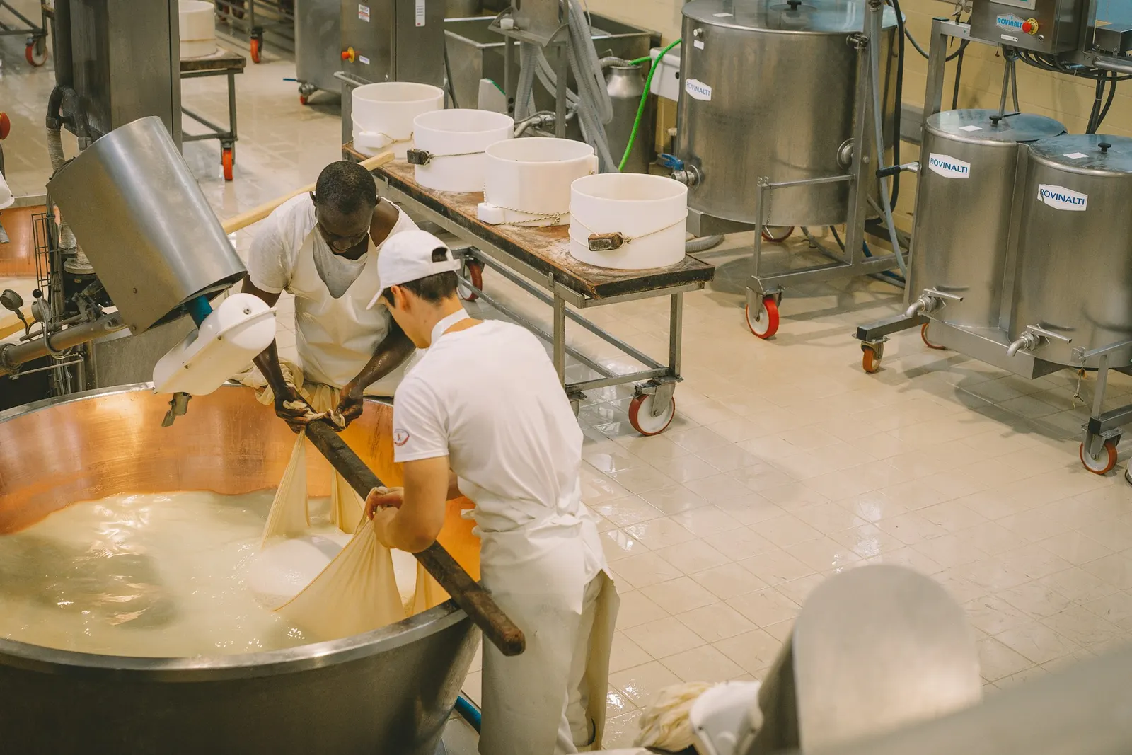 Fromagers en tenue blanche autour de cuves en cuivre et de moules dans un laboratoire de transformation laitière